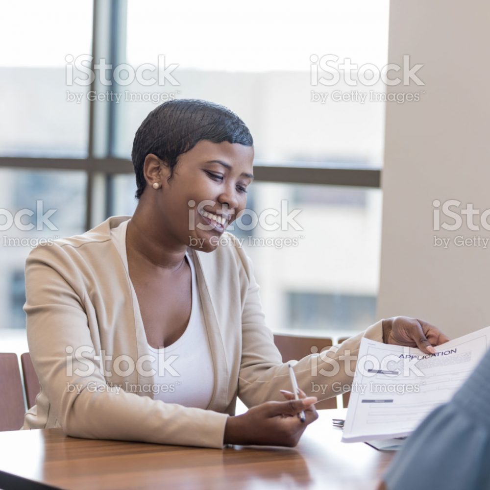 A female personal banker sits across a desk from her client and gestures to a banking application as she gives instructions.